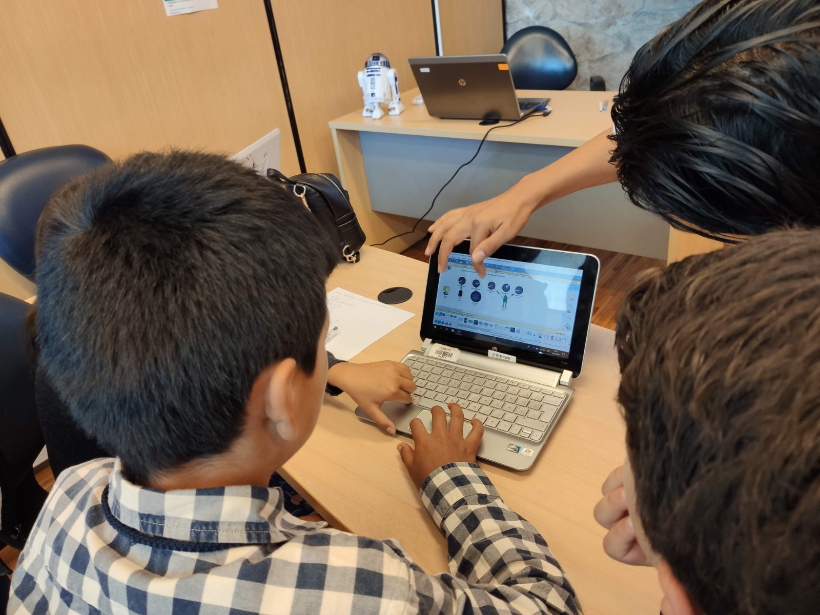 Estudiantes colaborando en un computador durante un taller de robótica de la Fundación REBDI, con un robot al fondo